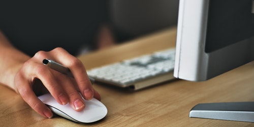 Close up of hand using a mouse next to computer screen and keyboard